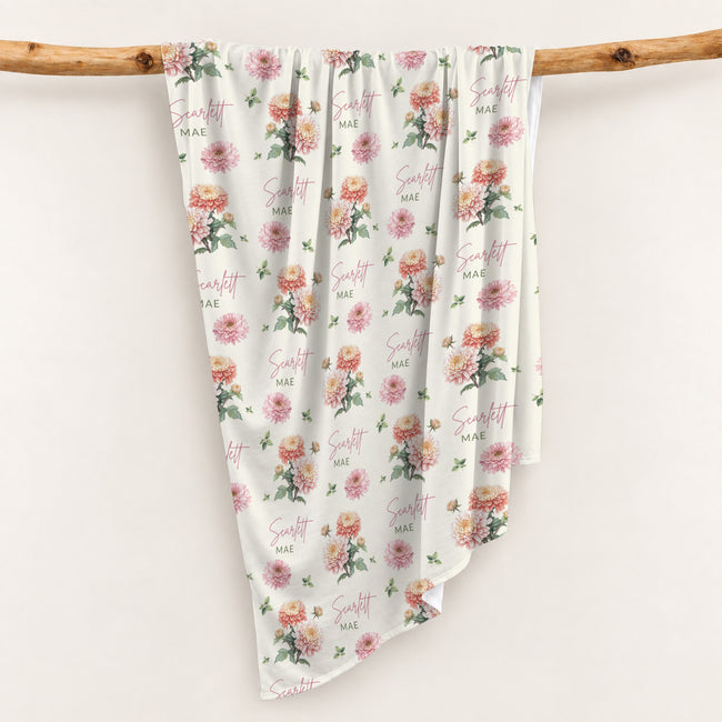 Ivory swaddle blanket with peach and pink chrysanthemums, green foliage, and the name Scarlett Mae in rose and green lettering.