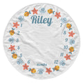 A circular white baby milestone chart blanket featuring colorful cartoon sea creatures and the name 'Riley' in blue script, with numbered months from 1 to 12 around the border.