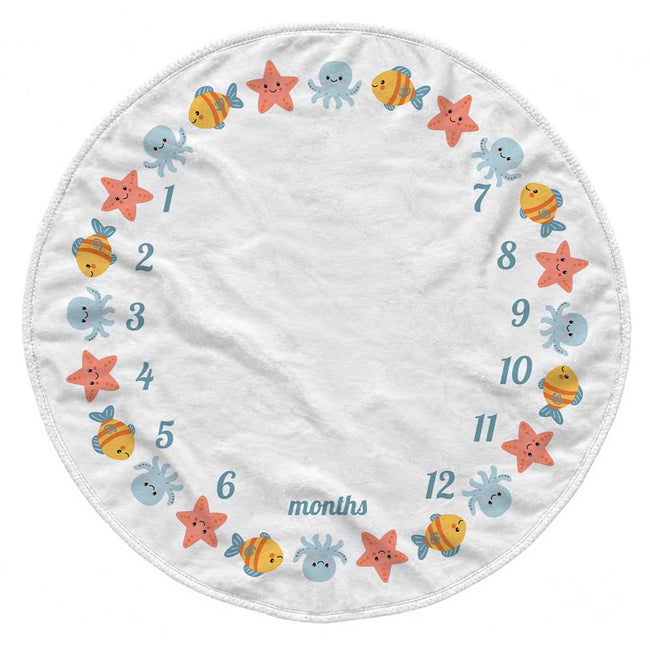 A round white baby growth chart blanket featuring colorful cartoon sea creatures like fish, starfish, octopus, and shrimp arranged around a circular timeline labeled 1 through 12 months.