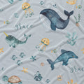 Light gray fabric with a watercolor-style ocean print featuring a blue whale, blue dolphin, teal narwhal, yellow jellyfish, seashells, coral, and the word Grace repeated in script.