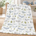 A white baby blanket draped over a woven basket, featuring a repeating pattern of light blue whales, green leaves, and the names 'Riley' printed in blue. The blanket is styled in a bright, modern nursery setting.