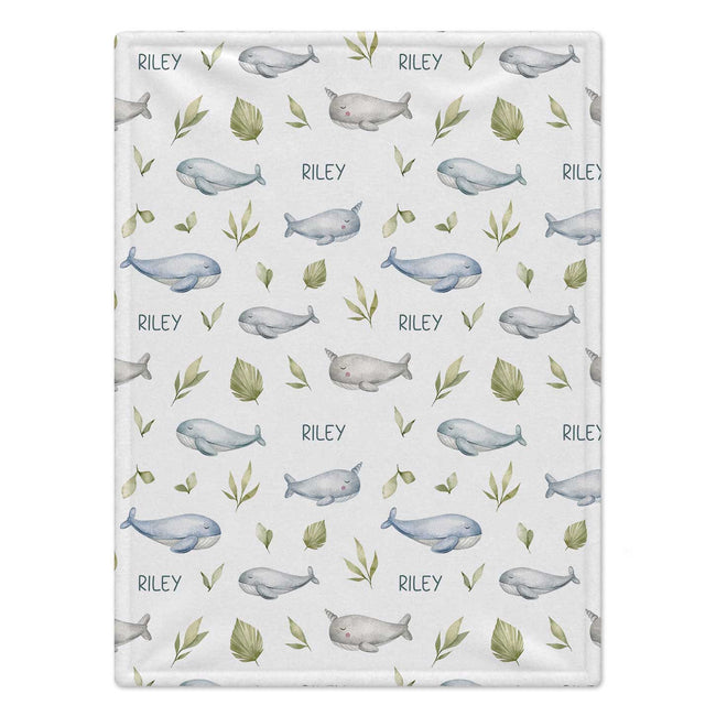 A personalized baby blanket featuring a repeating pattern of blue and gray whales, green leaves, and the name 'RILEY' printed in dark gray on a light gray background.