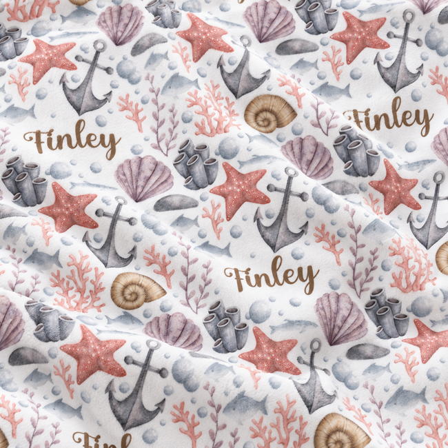 A close-up of a fabric or wallpaper pattern featuring an ocean theme with anchors, starfish, seashells, coral, and seashells in muted coral, gray, and brown tones on a white background, with the name 'Finley' printed in brown script.