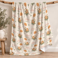 Cream blanket with golden-orange marigold clusters, scattered green leaves, and the name Autumn Grace in orange and green.