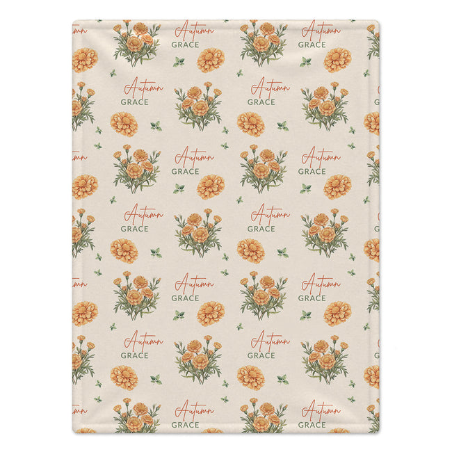 Cream blanket with golden-orange marigold clusters, scattered green leaves, and the name Autumn Grace in orange and green.