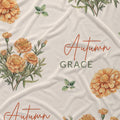 Cream fabric with golden-orange marigold clusters, scattered green leaves, and the name Autumn Grace in orange and green.