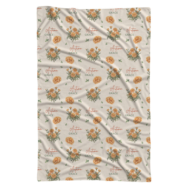 Cream swaddle blanket with golden-orange marigold clusters, green leaves, and the name Autumn Grace in orange and green.