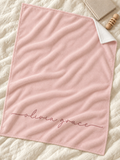 A soft pink baby blanket with the name 'olivia grace' embroidered in cursive at the bottom, styled on a textured cream quilted blanket with a wooden teething ring and a folded beige cloth nearby.