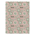 A personalized dog blanket featuring a repeating pattern of green paw prints and the name 'Rosie' on a dusty pink background.