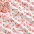 White fabric with a repeating pattern of pink butterflies and the word 'Emery' in pink script, shown close up with a plush pink butterfly toy partially visible in the top left corner.