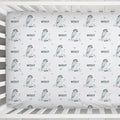 A white crib mattress fitted sheet featuring a repeating pattern of penguin illustrations, small birds, and the name 'WESLEY' printed in dark gray.