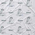 A white fabric with a repeating pattern of penguin illustrations, the name 'WESLEY' in dark gray text, and small bird silhouettes.