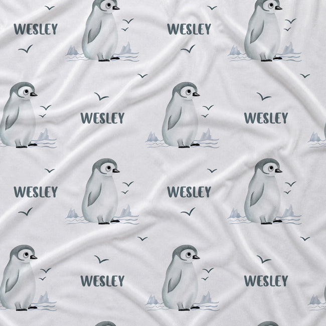 A white fabric with a repeating pattern of penguin illustrations, the name 'WESLEY' in dark gray text, and small bird silhouettes.