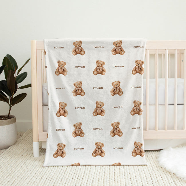 Full view of a personalized teddy bear blanket with repeating brown watercolor bears, bows, and the name Rowan on white.