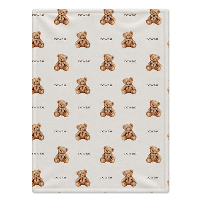 Teddy bear baby blanket personalized with Rowan, displayed over a natural wood crib in a neutral nursery.