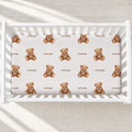 Personalized teddy bear crib sheet with brown watercolor bears, beige bows, and the name Rowan, shown in a white crib.