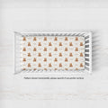 A top-down view of a white wooden baby crib containing a fitted sheet with a repeating pattern of small brown teddy bears and the word 'Rowan' printed underneath each bear.