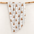 Personalized teddy bear swaddle blanket with the name Rowan and brown watercolor bears, draped over a wooden branch.