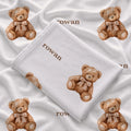 Folded teddy bear swaddle blanket showing the name Rowan in brown and watercolor bears wearing beige bows on white fabric.