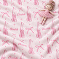 A close-up of a soft pink blanket or fabric with an allover ballet theme print, including pink pointe shoes, bows, small hearts, and the name 'Elizabeth' repeated in script. A small doll in a pink tutu lies on top of the fabric.
