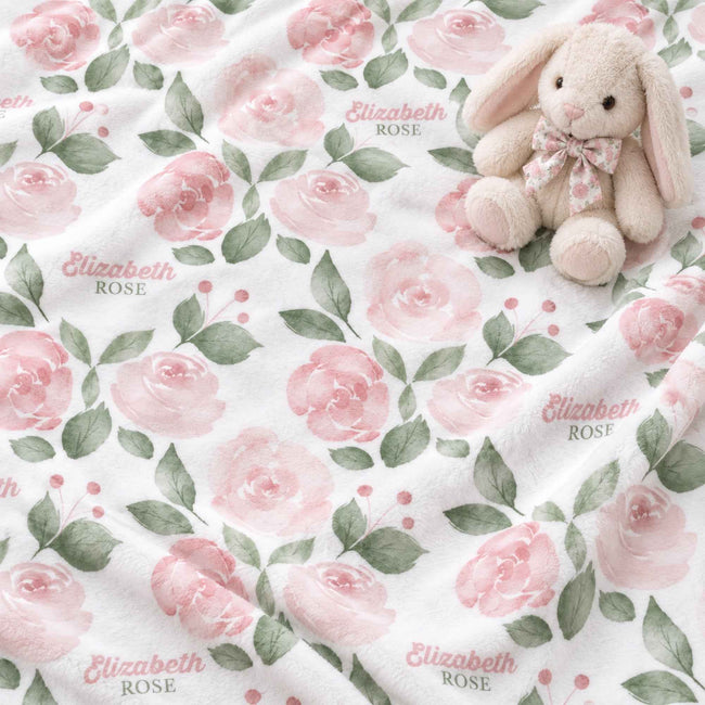 A soft plush blanket with a repeating pattern of pink roses, green leaves, and the text 'Elizabeth ROSE' on a white background, styled with a small stuffed bunny toy.