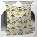 A fleece throw blanket with a colorful dinosaur pattern is draped over the headboard of a white bed.
