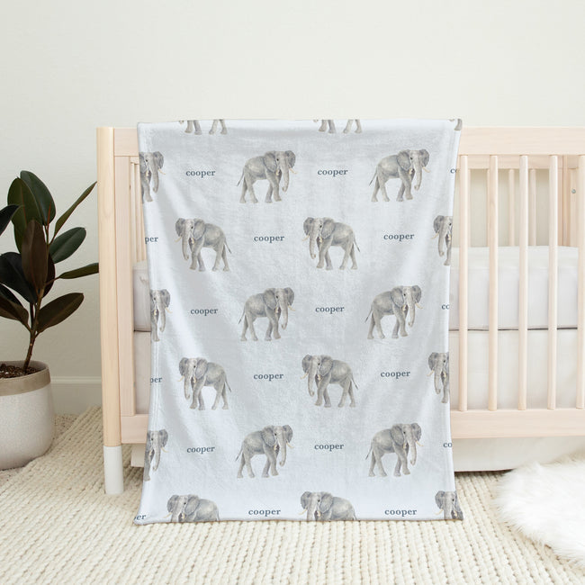 Little Elephant baby blanket personalized with Cooper, draped over a natural wood crib in a neutral nursery.