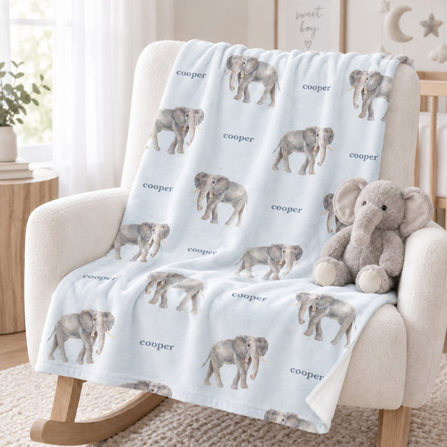 Pale blue Little Elephant blanket personalized with Cooper, draped over a cream rocking chair beside a plush elephant.