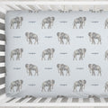 A white wooden crib with a fitted sheet featuring a repeating pattern of gray elephants and the word 'Cooper' in gray text, photographed from above on a light textured floor.