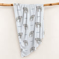 Little Elephant swaddle blanket with gray watercolor elephants and the name Cooper on pale blue, draped over a wooden branch.