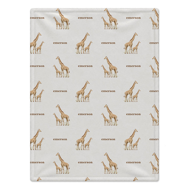 A personalized baby blanket with a repeating pattern of brown giraffes and the name 'emerson' printed in brown on a light gray background.