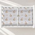 A changing table with a changing pad cover featuring a repeating giraffe and text pattern in brown and beige on a light gray background.
