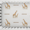 Little Giraffe personalized crib sheet featuring giraffe pairs and the name Emerson, shown close up in a white crib.