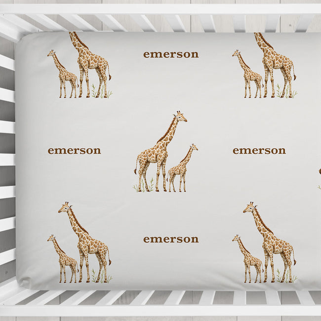 Little Giraffe personalized crib sheet featuring giraffe pairs and the name Emerson, shown close up in a white crib.