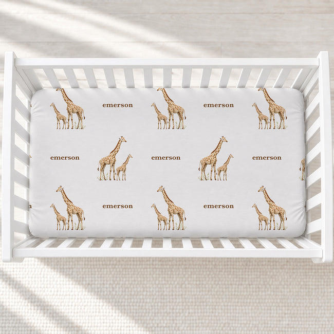 Overhead view of Little Giraffe personalized crib sheet with watercolor giraffe pairs and the name Emerson in a white crib.