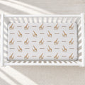 A white wooden crib with a fitted sheet featuring a repeating pattern of brown giraffes and the word 'Emerson' in brown text, shown from a top-down angle on a light textured floor.