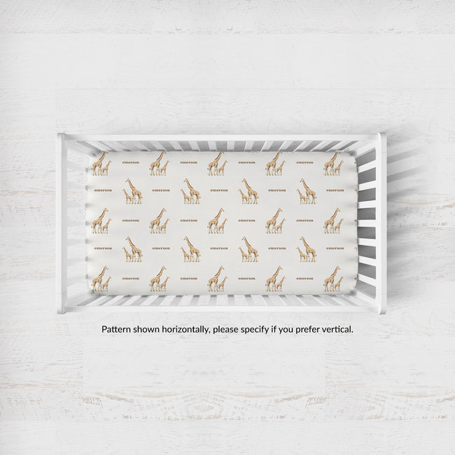A white wooden crib with a fitted sheet featuring a repeating pattern of brown giraffes and the word 'Emerson' in brown text, shown from a top-down angle on a light textured floor.