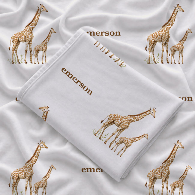 Folded Little Giraffe personalized swaddle blanket showing watercolor giraffe pairs and the name Emerson in brown on white.