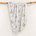 Little Giraffe swaddle blanket personalized with Emerson, draped over a wooden branch to display the repeating giraffe pattern.