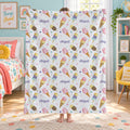 A person standing in a child's bedroom holding up a white fleece blanket with a colorful ice cream cone pattern and the name 'Abigail' repeated across it.