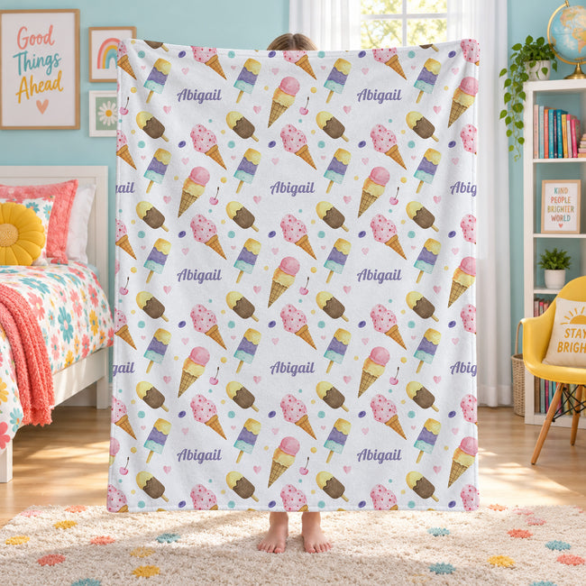 A person standing in a child's bedroom holding up a white fleece blanket with a colorful ice cream cone pattern and the name 'Abigail' repeated across it.