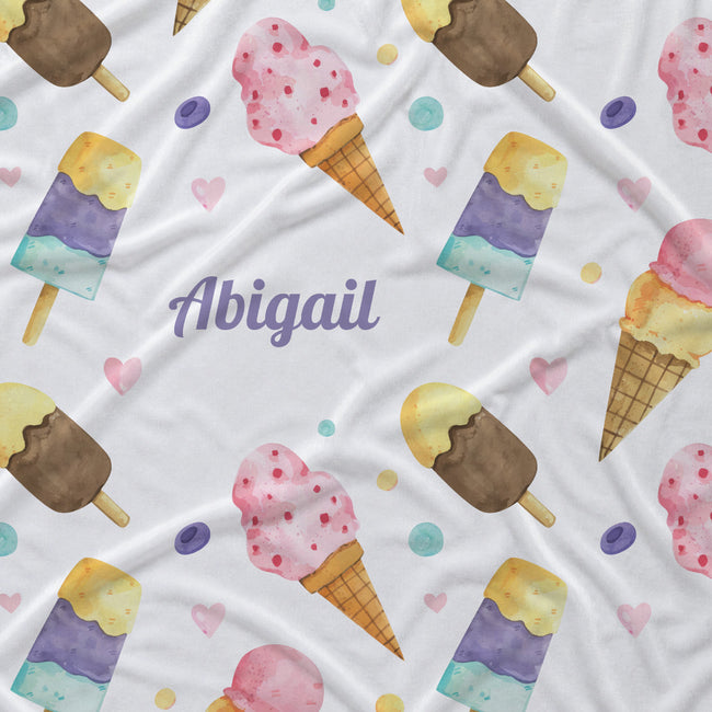 A white fabric blanket or throw featuring a watercolor-style repeating pattern of ice cream cones, popsicles, pink hearts, and small pastel dots, with the name 'Abigail' printed in purple script near the center.