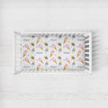 A white wooden baby crib with a custom printed mattress protector featuring a colorful ice cream cone pattern and the name 'Abigail' repeated in purple script, set against a white wood-paneled background.