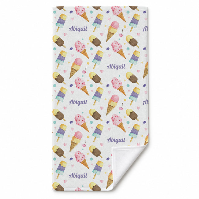 A personalized beach towel with a repeating ice cream cone and popsicle print, plus the name 'Abigail' repeated in purple script. The product is shown flat against a white background with one corner folded over to reveal the white reverse side.