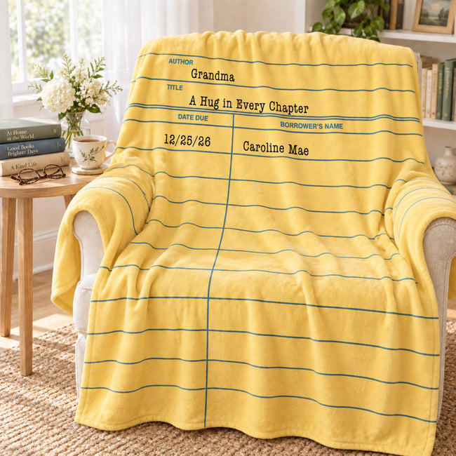 A yellow fleece throw blanket with blue horizontal lines and a lined-paper style writing template design, draped over a beige armchair in a bright, styled living room setting.