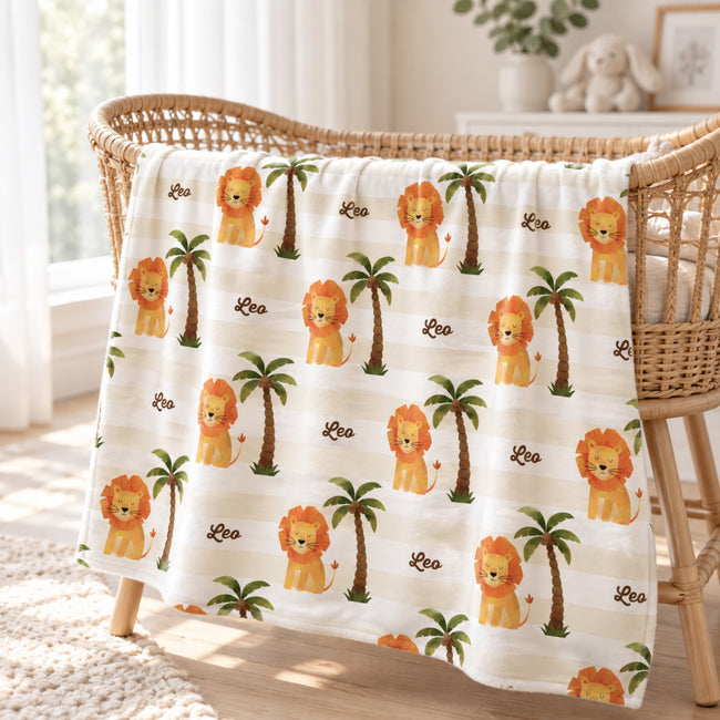 Little Lion blanket personalized with Leo, featuring golden lions, green palms, and cream stripes, draped over a woven bassinet.