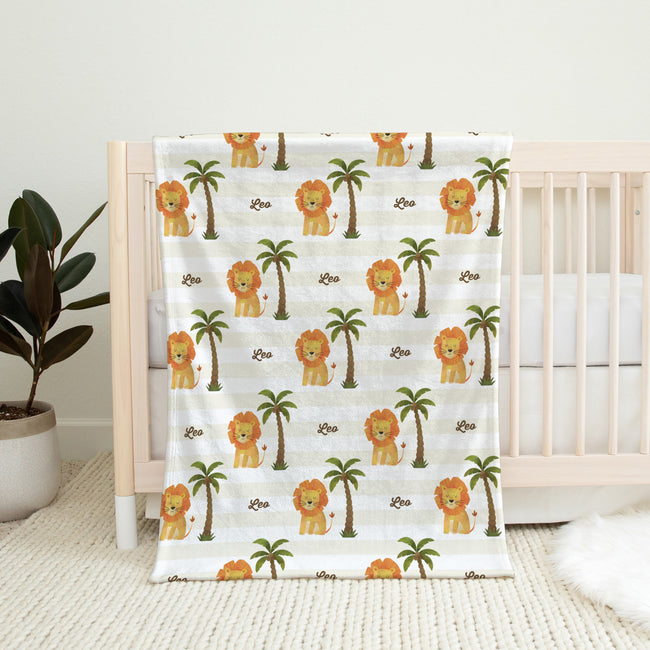 Little Lion personalized baby blanket with lions, palm trees, and the name Leo, displayed over a natural wood crib.