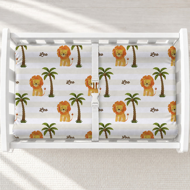 Little Lion changing pad cover with golden lions, green palms, cream and white stripes, and the name Leo, shown on a white changing table.