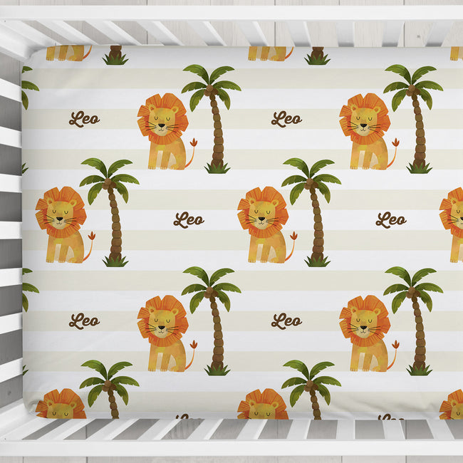 Close-up of Little Lion crib sheet showing orange-maned lions, green palm trees, and Leo in brown script over cream and white stripes.