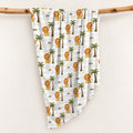 Little Lion swaddle blanket personalized with Leo, featuring golden lions, green palms, and cream stripes, draped over a wooden branch.